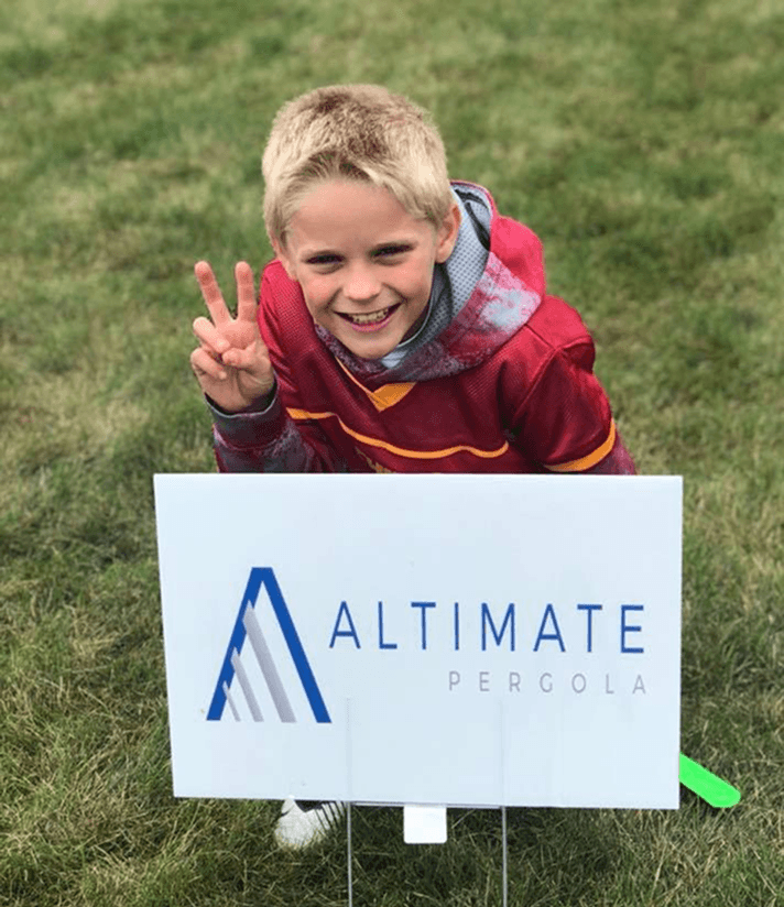 Child Smiling Behind Altimate Sign